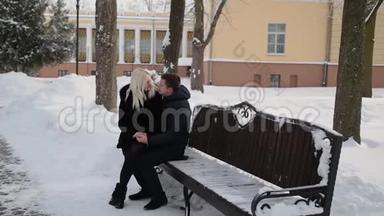 美丽的年轻夫妇坐在长凳上拥抱在一个城市冬季公园里说话和微笑。
